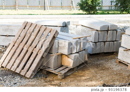 Reinforced concrete blocks neatly stacked on the territory of a fenced construction site, a curb stone on wooden pallets for road repairs 93196378