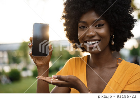 Portrait of a smiling young african woman holding blank screen mobile phone standing in the street Portrait of a smiling young african woman holding blank screen mobile phone standing in the street 93196722