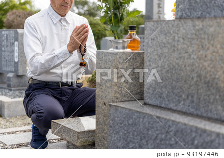 お墓参りをして手を合わせているシニア男性 93197446