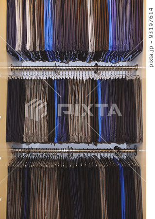 Showcase with many men's trousers hanging on hangers in stock on hangers in a men's clothing store Showcase with many men's trousers hanging on hangers in stock on hangers in a men's clothing store 93197614