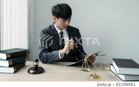 The man lawyer is sitting at the desk in the office with a justice scale and gavel hammer. 93198061