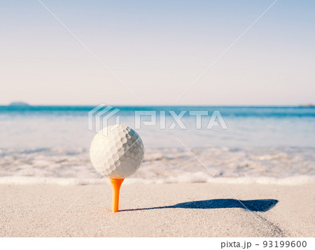 The golf ball is on the tee, embroidered on the sand beach with the sea in the background The golf ball is on the tee, embroidered on the sand beach with the sea in the background 93199600