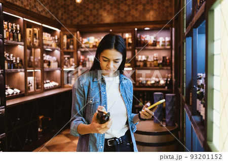 Portrait of young woman buying wine in an liquor store Portrait of young woman buying wine in an liquor store 93201152