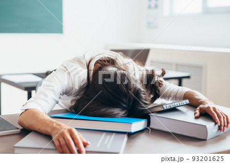 Tired female student sleeping on desk face and hands on books 93201625