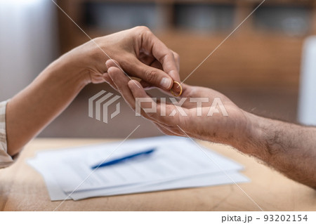 Hand of adult caucasian female gives ring to her ex husband at table with divorce papers, close up, cropped Hand of adult caucasian female gives ring to her ex husband at table with divorce papers, close up, cropped 93202154