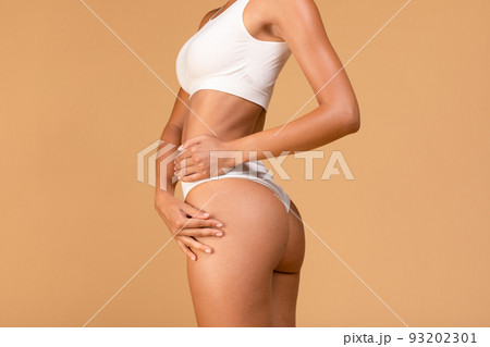 Bodycare concept. Young half-turned lady demonstrating her perfect hips, wearing white lingerie, beige background 93202301