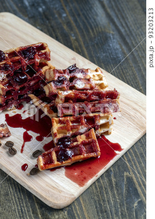 soft waffles with red cherry jam on a serving board 93203213