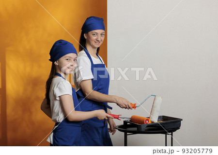 Portrait of family painting orange walls, using paintbrush and tools to redecorate home apartment. Mother and small girl renovating house with paint color and diy renovation equipment. Portrait of family painting orange walls, using paintbrush and tools to redecorate home apartment. Mother and small girl renovating house with paint color and diy renovation equipment. 93205779