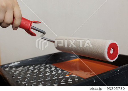 Woman using roller paintbrush and orange color to paint apartment walls, working on house redecoration with painting tools and dye container. Holding round brush with bristles. Close up. Woman using roller paintbrush and orange color to paint apartment walls, working on house redecoration with painting tools and dye container. Holding round brush with bristles. Close up. 93205780