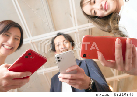 スマホを近づけて笑顔を見せる3人の男女 93210349