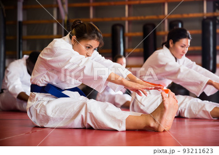 Man and woman in kimono warming up before karate training. They're doing stretching exercises for legs 93211623