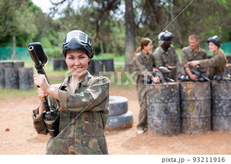 Smiling woman wearing uniform and holding gun ready for playing paintball with friends 93211916