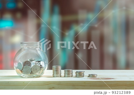 Saving money and investment concept, Coins in glass bottle for savings and stack coins to show increase of savings money on wooden table, graphs and index blurred background. 93212389