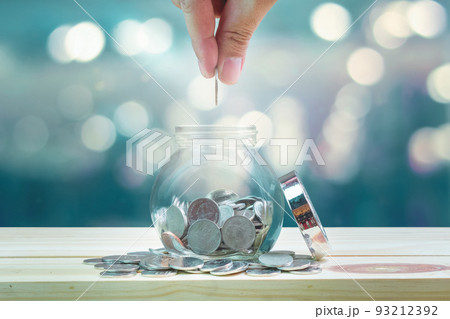 Saving money and investment concept, hand putting coin in glass bottle for savings which on wooden table and bokeh background. 93212392