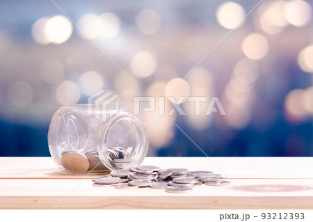 Concept saving and financial with coins spilling out of a glass bottle on wooden table and bokeh background. 93212393