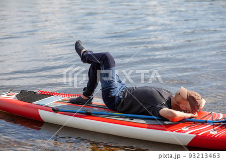 SUP board Stand up paddle man boarding on lake standing happy on blue water. A man swims and rests on a SUP board on the river SUP board Stand up paddle man boarding on lake standing happy on blue water. A man swims and rests on a SUP board on the river 93213463