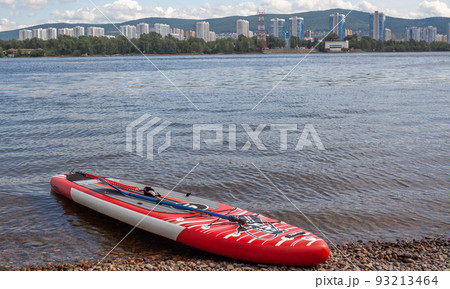 12.07.2022 Krasnoyarsk, Russia. Red SUP board on the river bank. Paddle board on the lake shore. Supboard water tourism and active sports. 12.07.2022 Krasnoyarsk, Russia. Red SUP board on the river bank. Paddle board on the lake shore. Supboard water tourism and active sports. 93213464