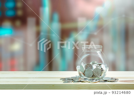 Saving money and investment concept, Coins in glass bottle for savings which on wooden table, graphs and index blurred background. Saving money and investment concept, Coins in glass bottle for savings which on wooden table, graphs and index blurred background. 93214680