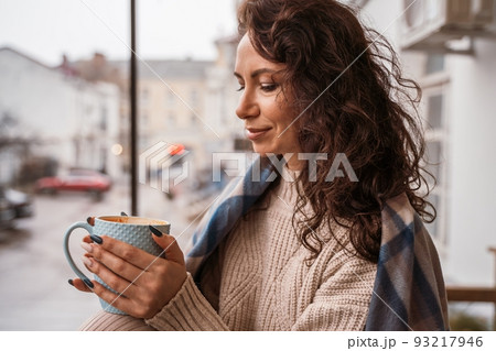 A middle-aged woman in a beige sweater with a blue mug in her hands is in a street cafe on the veranda A middle-aged woman in a beige sweater with a blue mug in her hands is in a street cafe on the veranda 93217946