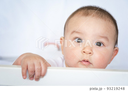 Cute portrait of a baby in a crib close-up. A child in white clothes on white underwear. Tenderness and care, children's problems. 93219248