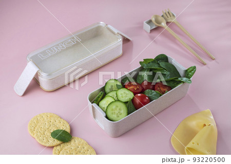 Office or school vegetarian lunch box. Cucumber, tomato, spinach, cookie, cheese lunch box on light background high angle view 93220500