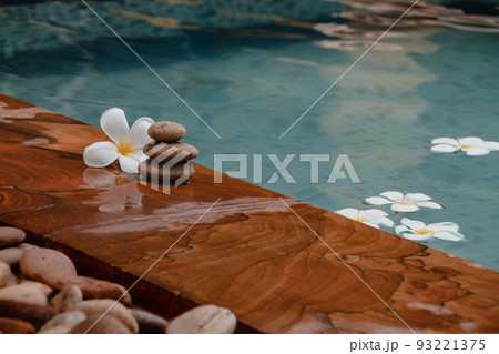 Stack of flat stones with a frangipani flower beside a swimming pool 93221375
