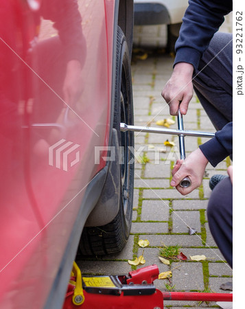 A wrench in the hands of an auto mechanic unscrews the bolts and nuts of a car wheel. Autumn day. A wrench in the hands of an auto mechanic unscrews the bolts and nuts of a car wheel. Autumn day. 93221762