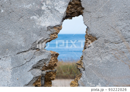 You can see the sea through a hole in the wall. Focus selective on the wall. Concept. A hole in the wall from a projectile You can see the sea through a hole in the wall. Focus selective on the wall. Concept. A hole in the wall from a projectile 93222026