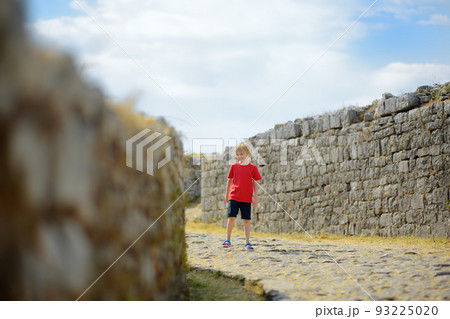 Little child tourist visits famous Fortress Rozafa near Shkodra city. Boy watching ancient stone walls and towers of bastion. Interest in history of children. Travel and tourism 93225020