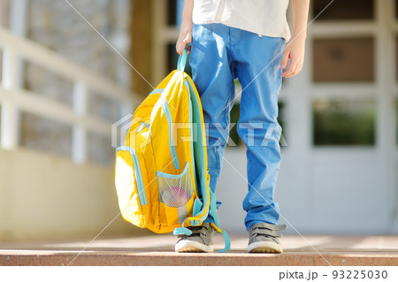Little student with a backpack on the steps of the stairs of school building. Close-up of child legs, hands and schoolbag of boy standing on staircase of schoolhouse.Back to school concept. 93225030