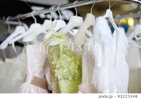 Few beautiful dresses on a hanger in wedding salon or atelier sewing studio. Wedding exhibition or shop, evening and bridesmaid dresses. Holiday clothes rental 93225348