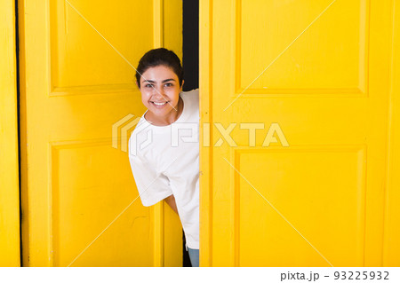 Young smiling indian woman peeking through yellow open door Young smiling indian woman peeking through yellow open door 93225932