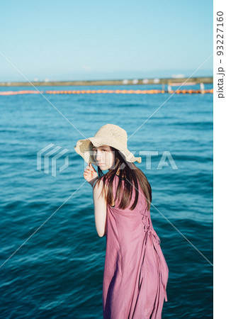 海辺で振り返る麦わら帽子の若い女性 海辺で振り返る麦わら帽子の若い女性 93227160