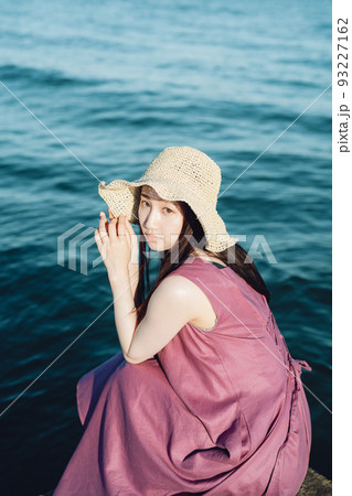 海辺で振り返る麦わら帽子の若い女性 海辺で振り返る麦わら帽子の若い女性 93227162
