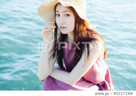 海のそばで座る麦わら帽子の若い女性 海のそばで座る麦わら帽子の若い女性 93227168