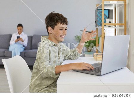 Cheerful boy who studies at home is talking to teacher or tutor using video call. 93234207