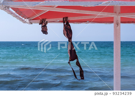 Marine background. On the beach, a swimsuit bra and shorts are hung under an umbrella. vacation freedom concept Marine background. On the beach, a swimsuit bra and shorts are hung under an umbrella. vacation freedom concept 93234239