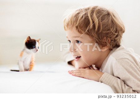 Child playing with kitten. Cat and kid at home. 93235012