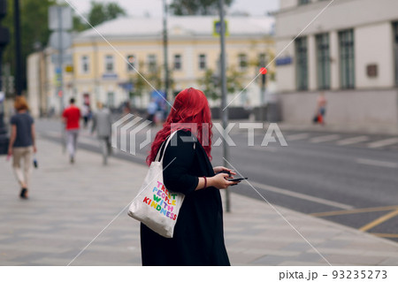 European plus size woman walking outdoor street city with mobile cellular phone. Young red pink haired body positive girl using cellphone smartphone 93235273