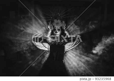 Woman with mexican skull halloween makeup in dark with backlight rays. Day of the dead aka Dia de los Muertos and halloween black and white concept. Woman with mexican skull halloween makeup in dark with backlight rays. Day of the dead aka Dia de los Muertos and halloween black and white concept. 93235968