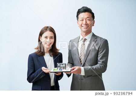 精巧な住宅模型を持つスーツ姿の男女 93236794