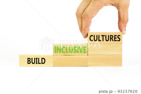 Build inclusive cultures symbol. Concept words Build inclusive cultures on wooden blocks. Businessman hand. Beautiful white background. Business build inclusive cultures concept. Copy space. 93237620