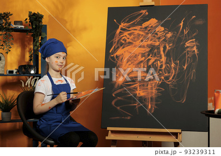 Portrait of young artist painting masterpiece with orange color from mixing tray and dye palette, creating art design on canvas with easel. Creative skills to paint colorful artwork with watercolor. Portrait of young artist painting masterpiece with orange color from mixing tray and dye palette, creating art design on canvas with easel. Creative skills to paint colorful artwork with watercolor. 93239311