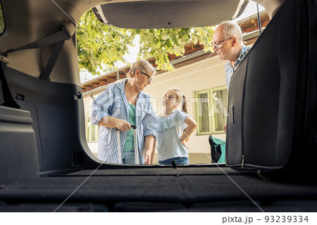 Grandparents and niece leaving on vacation, loading travel bags and baggage in automobile trunk. Senior people and little kid travelling on summer holiday road trip with vehicle, drive journey. Grandparents and niece leaving on vacation, loading travel bags and baggage in automobile trunk. Senior people and little kid travelling on summer holiday road trip with vehicle, drive journey. 93239334