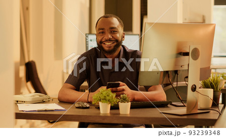 Portrait of african american man using smartphone app on computer, planning business presentation and doing research on social media network. Working with internet application on mobile phone. 93239348