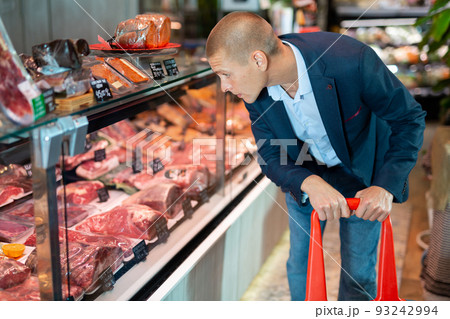 Focused man examines the production in the department of the butcher shop in the supermarket 93242994