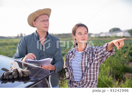 Farmers discussing documents near car on farm 93242996