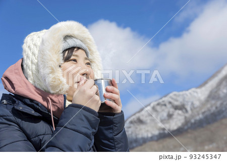 冬山でマグカップに入れたホットドリンクを飲む若い女性 93245347