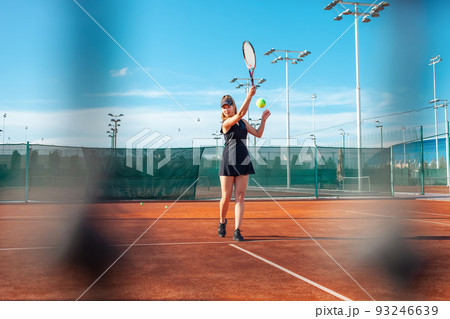 A beautiful young woman plays tennis on the court. Sunlight, training, competition. Outdoor sports, team play. Active lifestyle, athlete with a racket and a ball 93246639