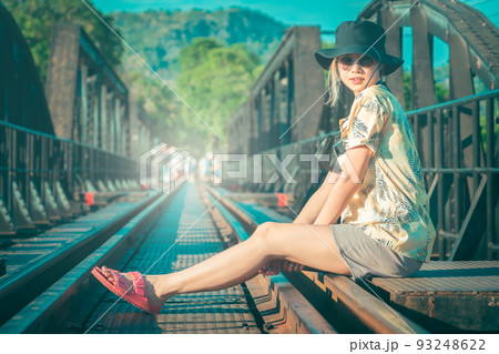 Female Asian tourist is sitting on the old train track of River Kwai Historical site in Kanchanaburi, Thailand. 93248622